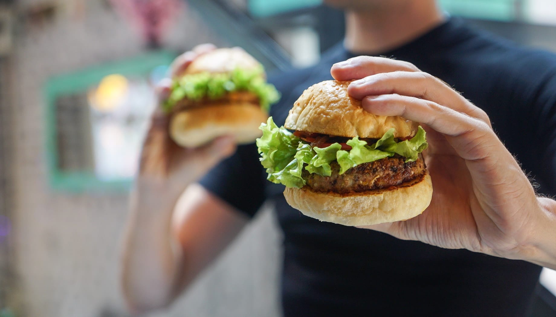 Man holding a hamburger with lettuce, tomato, and a roll.